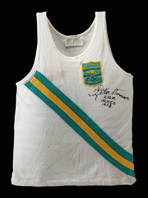 White singlet with green and gold across the chest, signed 'Peter Norman' on the left breast.