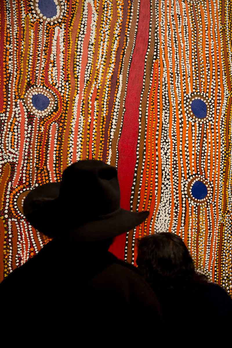 Silhouettes of two people facing a vibrant Australian Indigenous artwork.