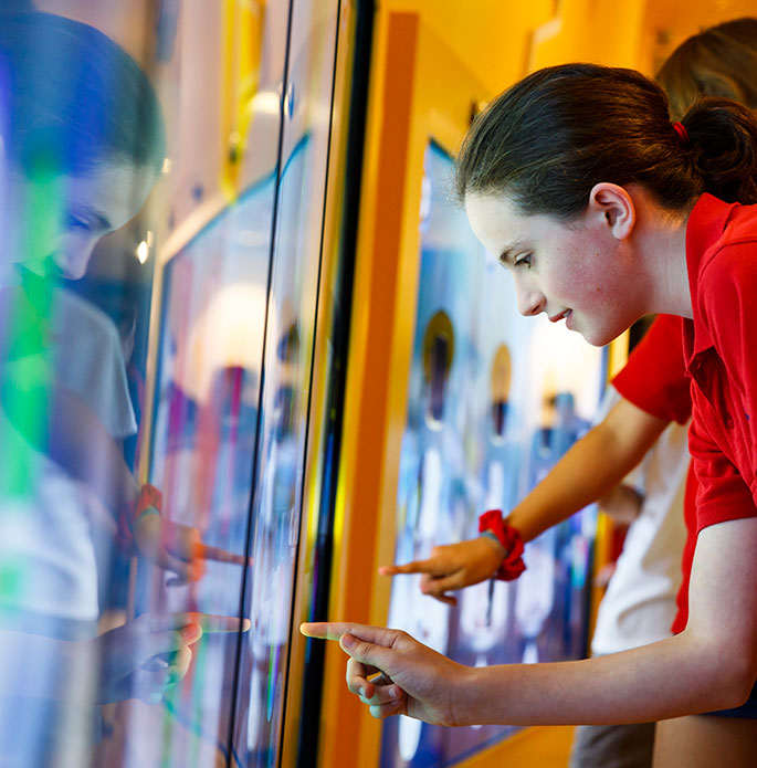 A girl leans forward to touch a screen.