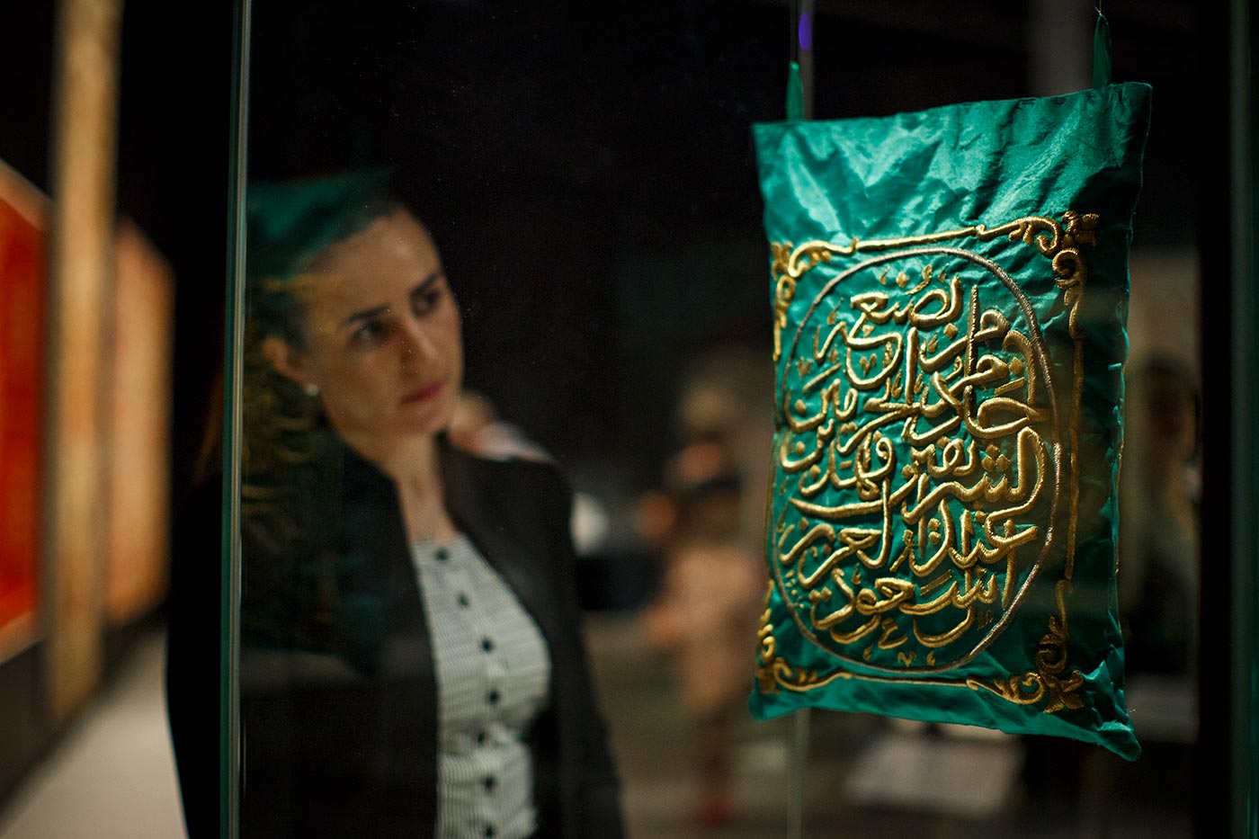 A woman looks at a green and gold object resembling a bag which hangs suspended.