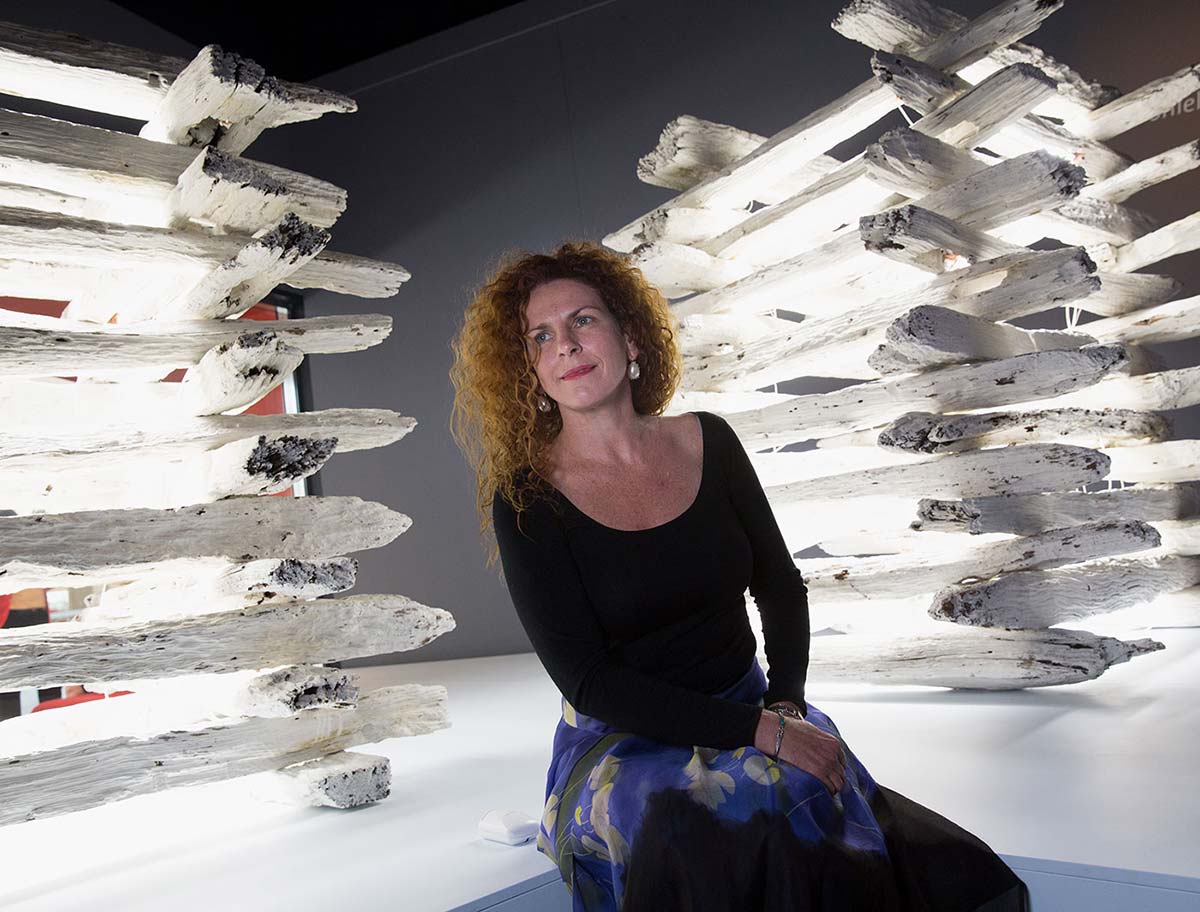 A woman sits between sculptural artworks of stacked white logs.