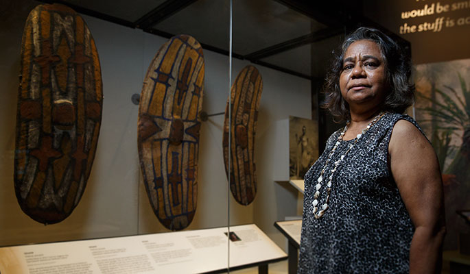 A woman stands beside a display case containing three shields and an old photograph.