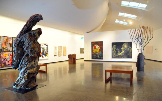 Interior view of an art gallery exhibition. A modernist sculpture is in the foreground.