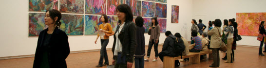 About 20 visitors in an art gallery with Emily Kngwarreye painting hanging in the background.